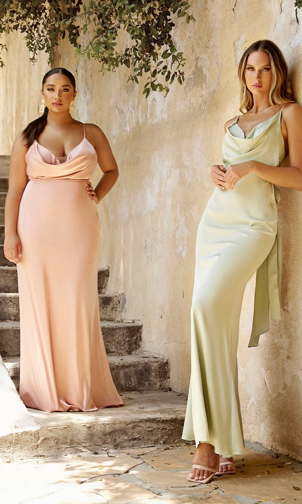 Two women stand outdoors against a beige wall with greenery above, wearing Tie-Back Long Prom Dress 7487 in blush pink and light green satin.